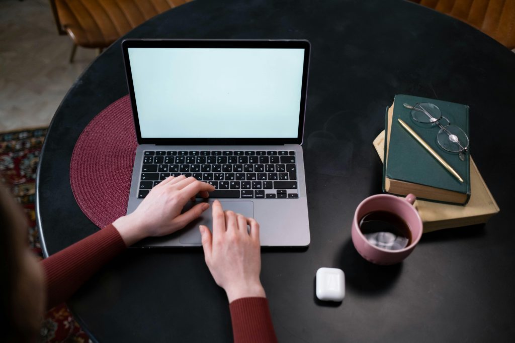 Hands typing on a laptop at a stylish indoor workspace with coffee and books.